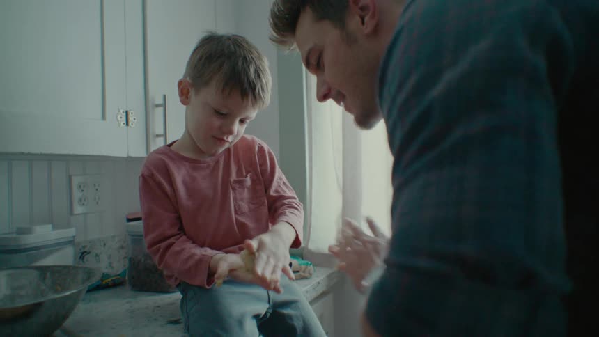Father and son molds flour while smiling inside the kitchen at midday