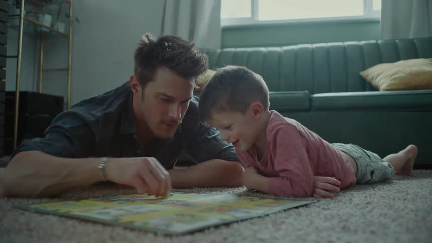 Father and son playing board game while laying on the floor indoor at midday