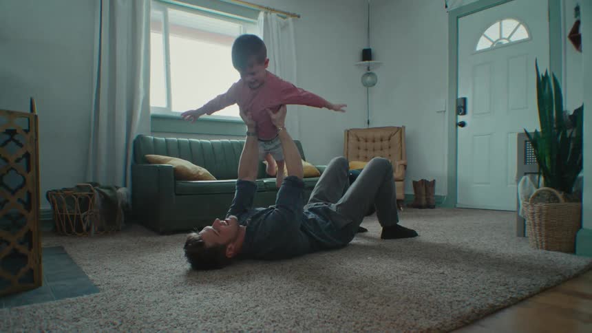 A man is lying on the floor playing airplane with his young son