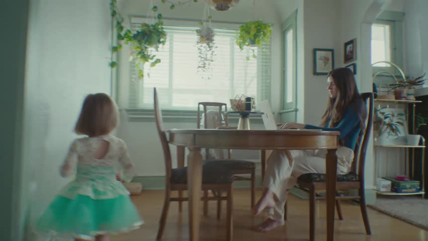 Two kids run past their mother in a dining room