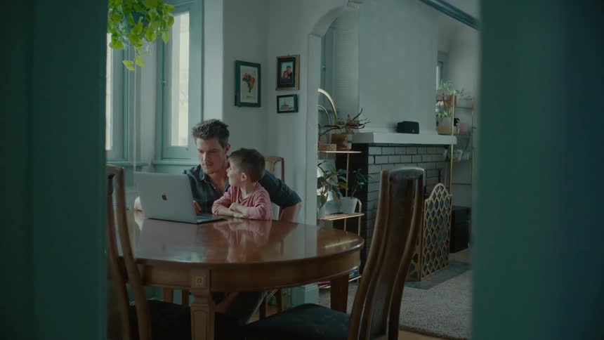 Father and son sit at dining table using laptop
