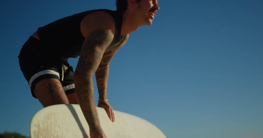 Man on the beach applying paraffin to his surfboard