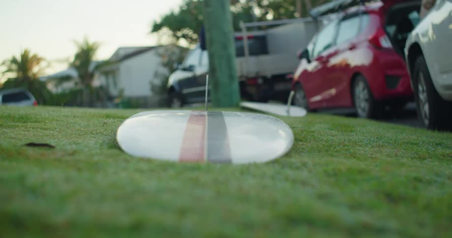 Surfboard lying in the middle of a lawn next to vehicles