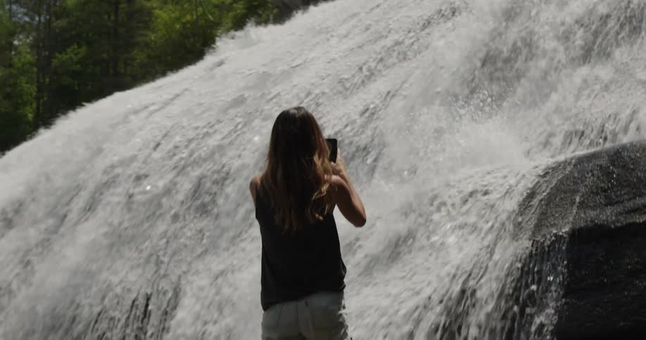 A woman is photographing the waterfall with her cell phone