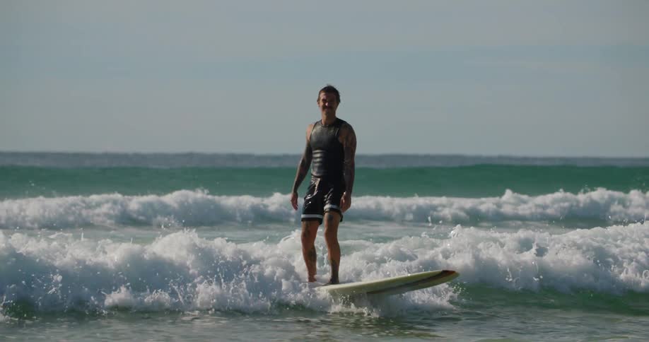 Young man rides a longboard over a wave near the shore