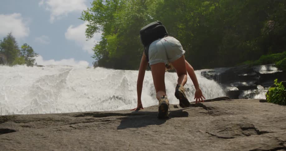A woman is crawling to climb a rock and when she climbs there is a huge waterfall