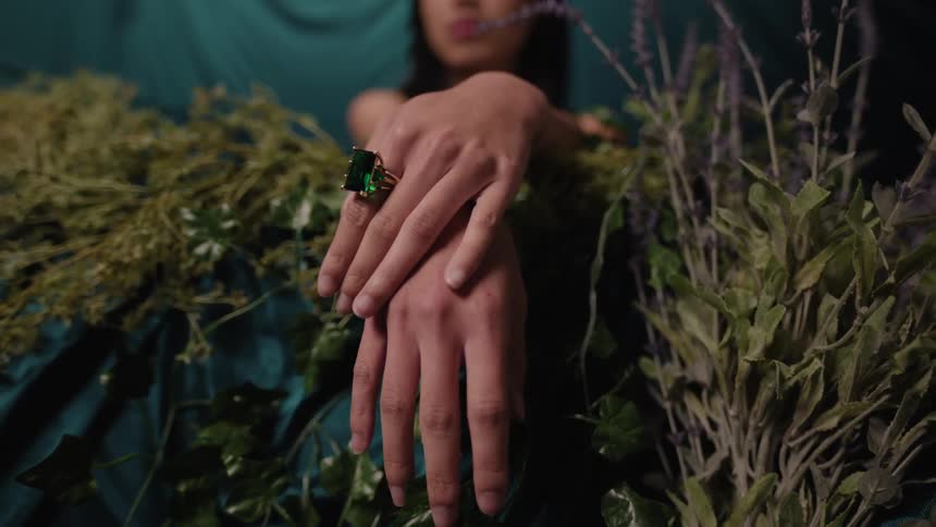Two female hands rest on a surface covered with green herbs