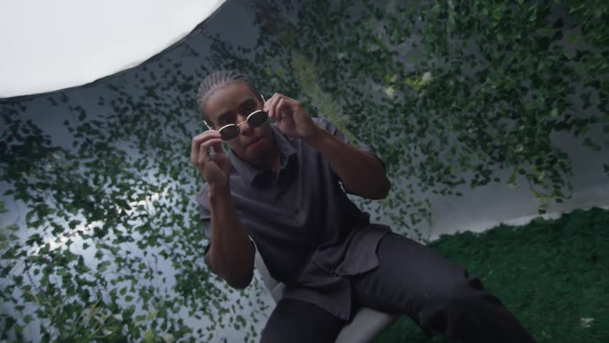 A black man sits in a chair and puts on sunglasses