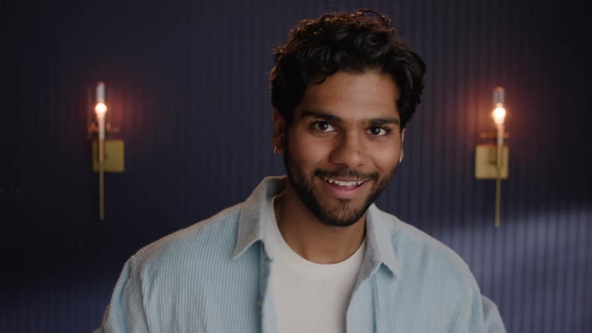 An indian man grins as he adjusts his shirt