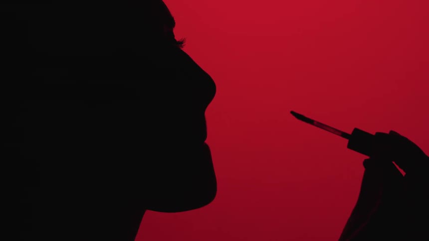 Silhouette of the side profile of a woman applying lip gloss