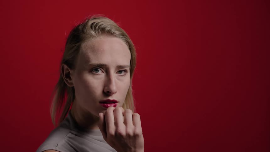 Portrait of a blonde woman using red lipstick and makeup on a red studio background