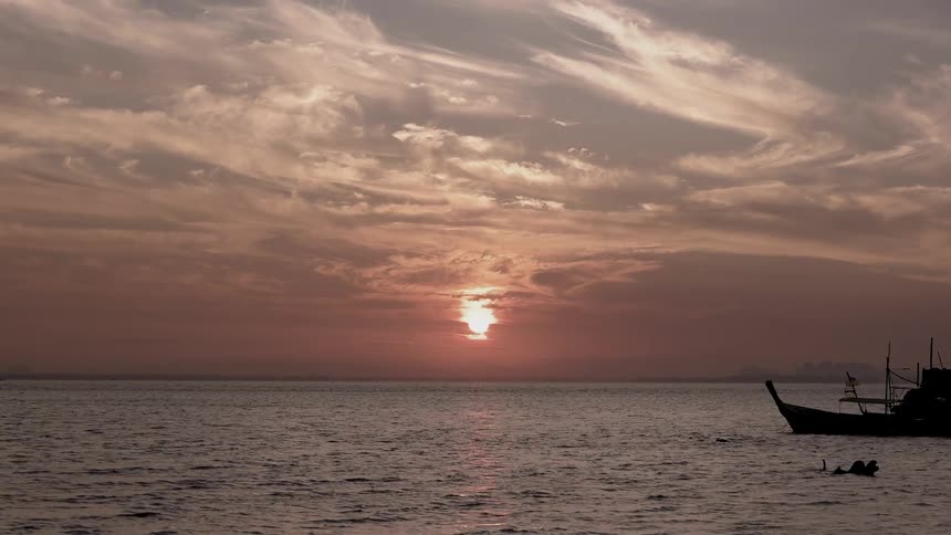 Boat anchored in a large body of water at sunset