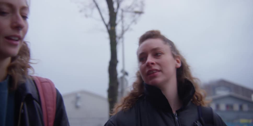 Two women talk to each other while walking down the street