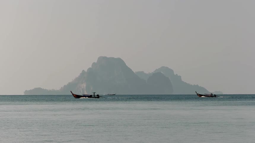Two boats moving across smooth waters with a mountainous island behind them
