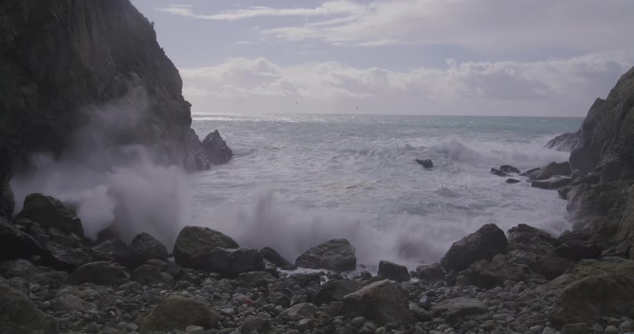 Waves splash against rocks along the coast as they roll into shore and seagulls fly