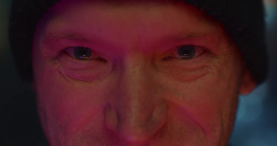 Close up of the eyes of a man under red lights inside a dark room
