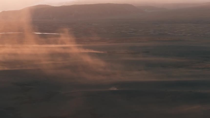 Aerial of vehicles driving through the desert during the cloudy dawn