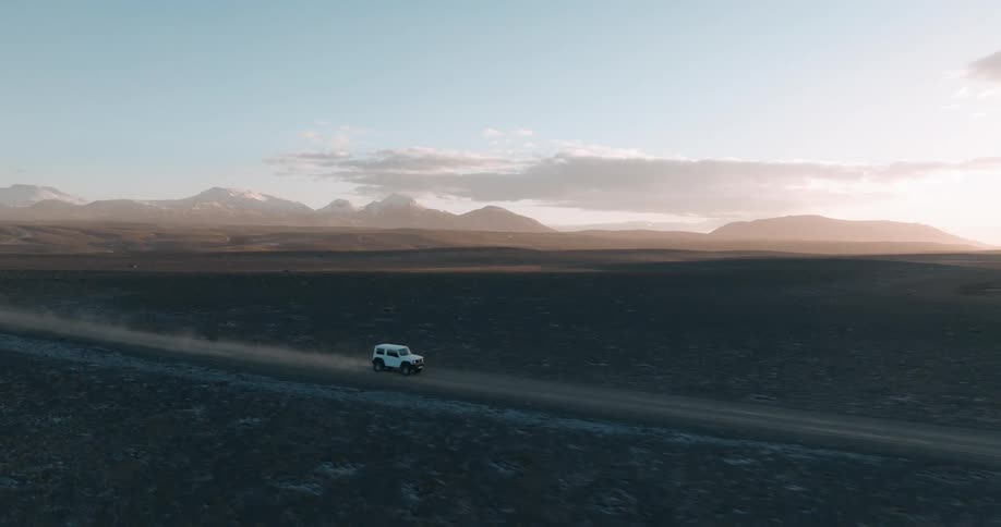 Aerial view of a white jeep driving on dirt road in the desert at sunset
