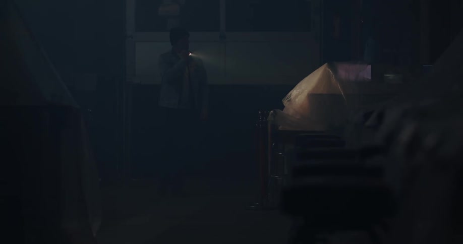 A man holding a torchlight looking around inside a warehouse at night