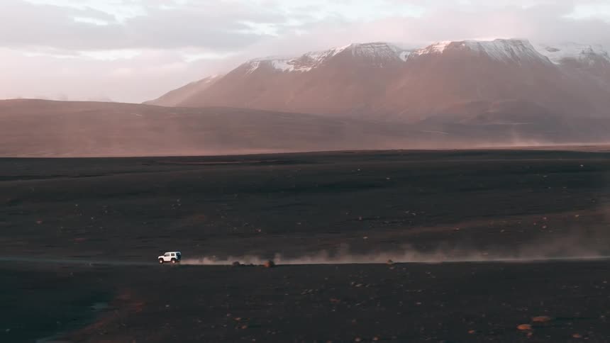 Jeep traveling at high speed across desert terrain with snowy mountain ranges in the background