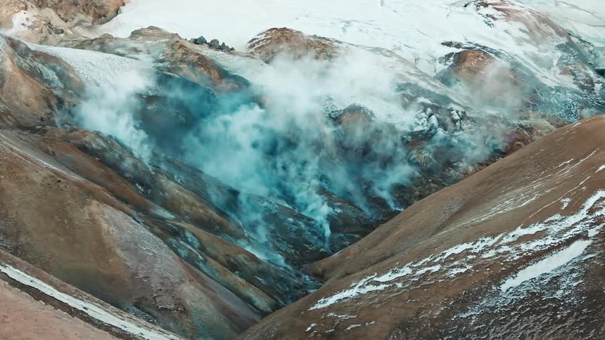 A rocky landscape with snow and steam rising from the ground