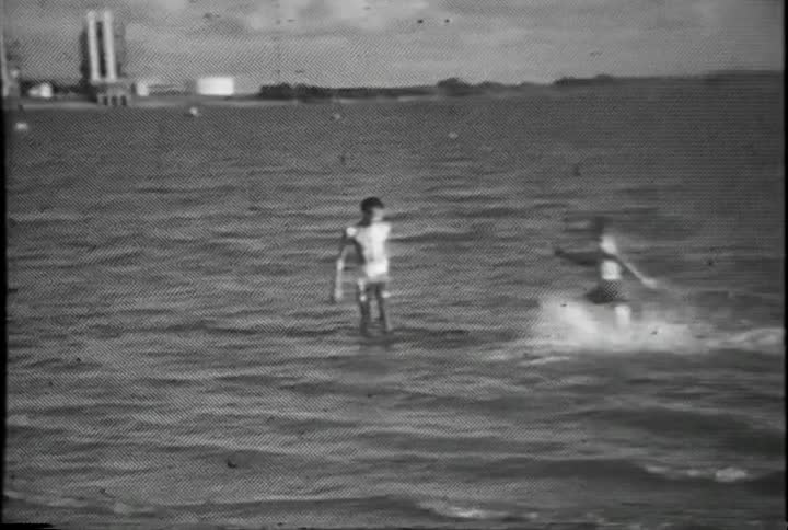 A boy mugging for the camera as he stands in the ocean is joined by another boy