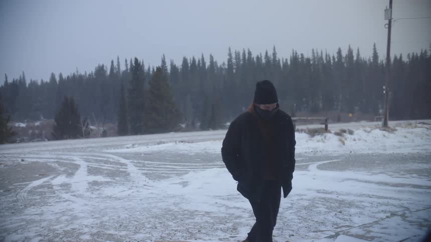 Man walking on a snowcovered street with forests behind him