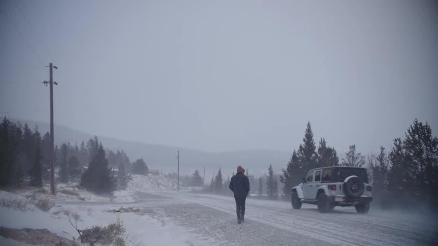 A man walking along a rural road during a blizzard when a car passes him by