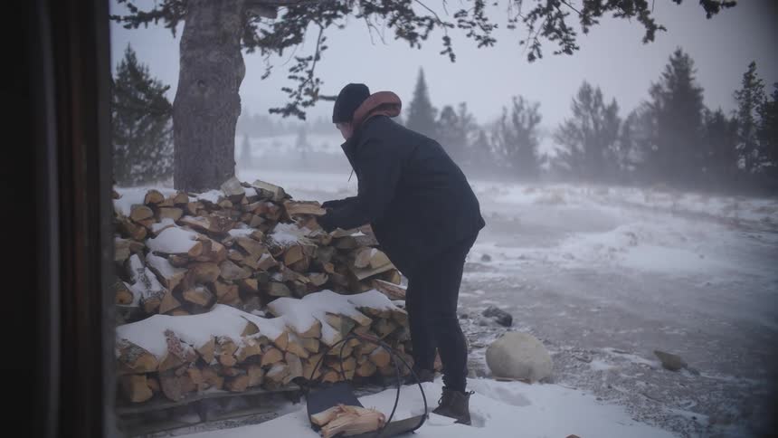 A man gathering wood for a fireplace in a basket while snowing