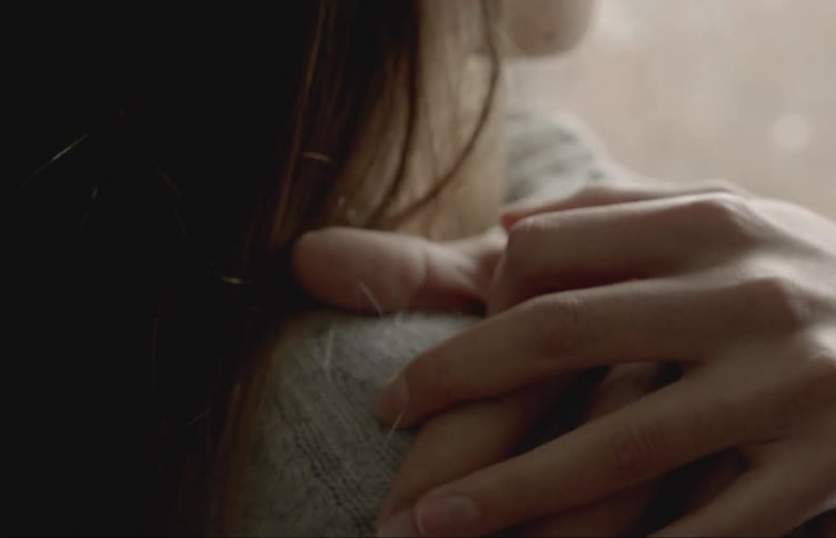 A closeup of two peoples hands touching gently on someones shoulder