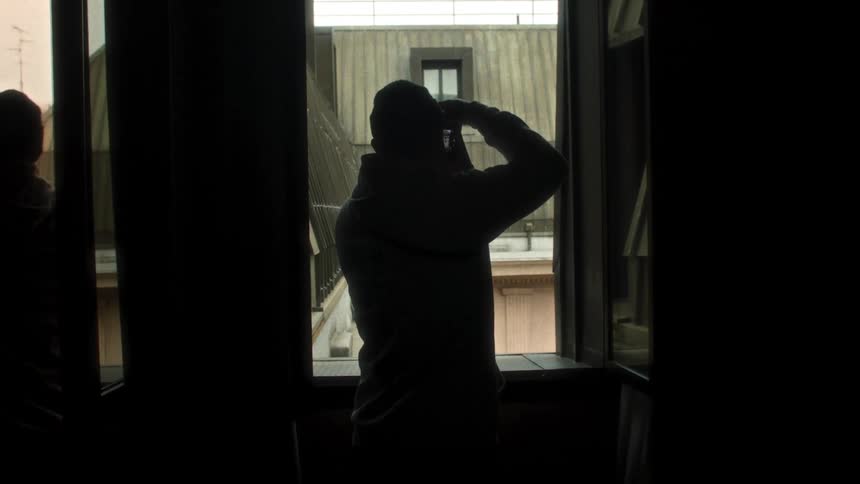 Man in the window of a building taking a photo with a camera