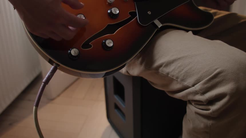A human hand plugging a cable into a brown guitar