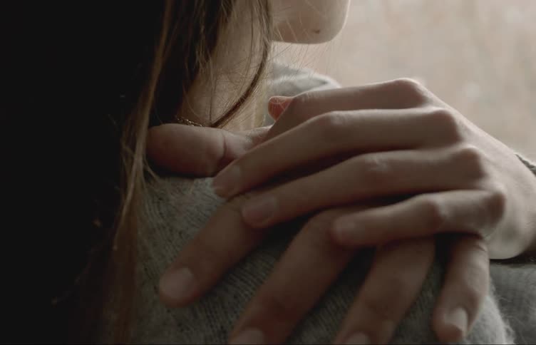 Closeup on the hands of a man hugging his wife who puts her hand on top of him