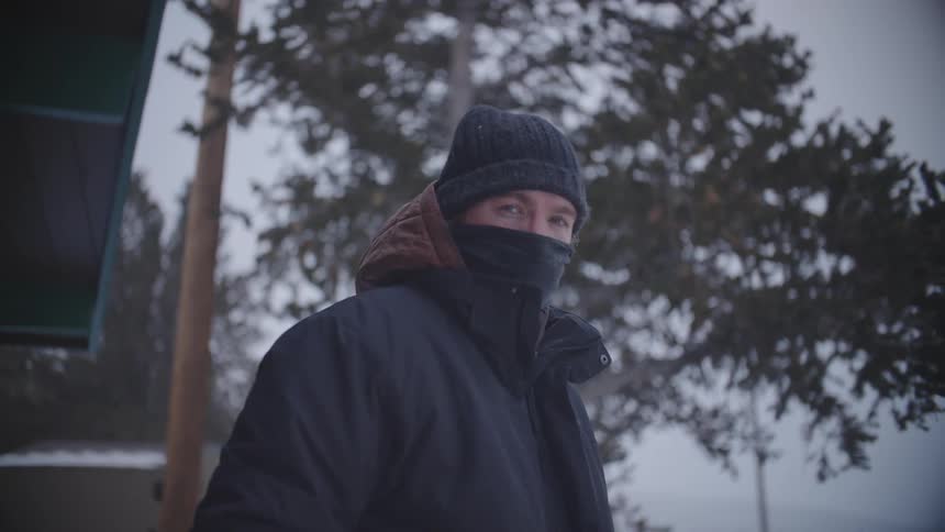 A man is wearing a coat and hat in a cold environment and his mouth is covered