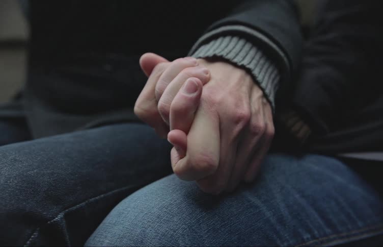 Two people sitting side by side hold hands tightly