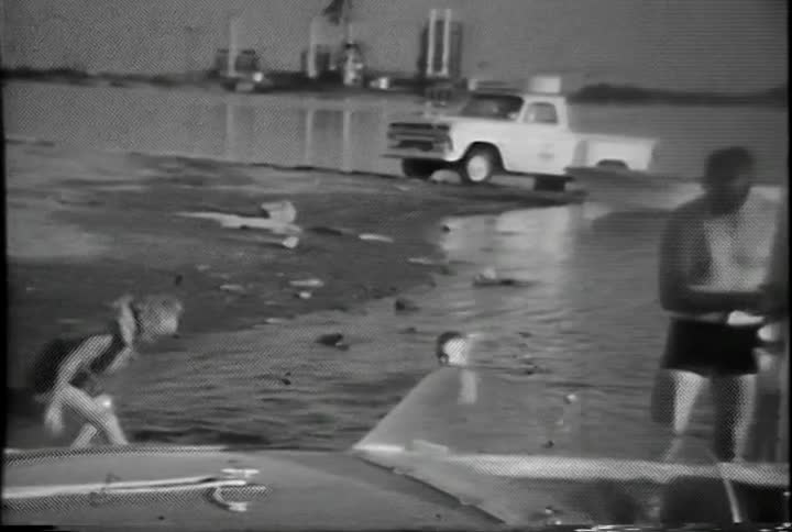 A little girl wearing a life vest gets out of the water and sits on the shore