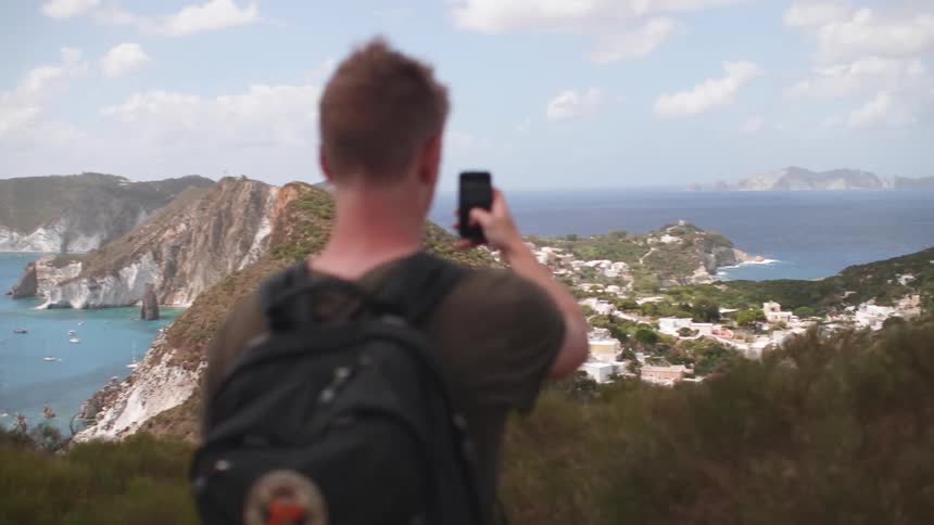 A man films a bay and island with a smart phone