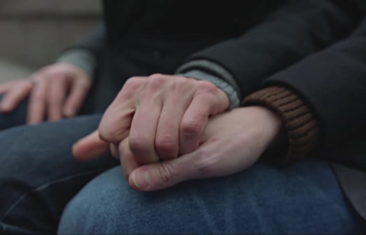 Closeup of two peoples holding hands wearing jackets and jeans