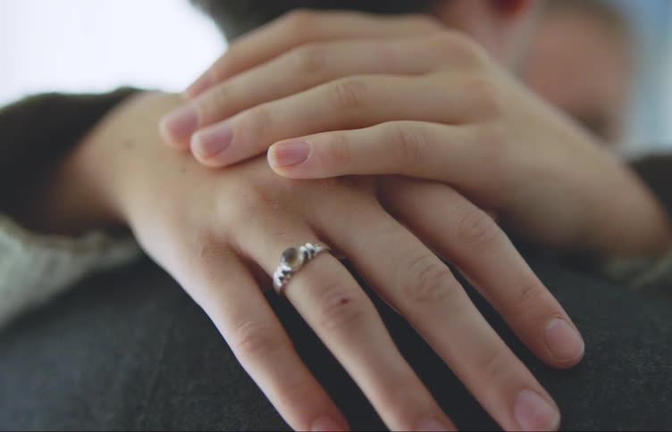 Closeup of a womans hands with a ring hugging the back of her partners neck