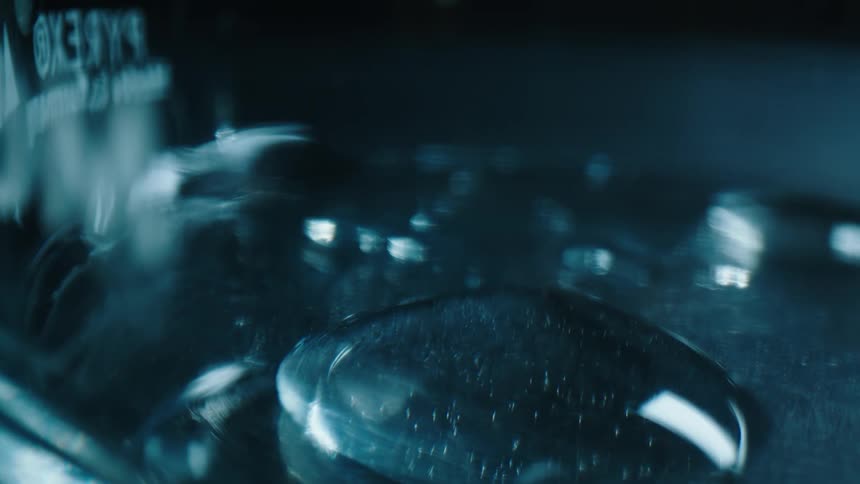 Several drops of water drip into a glass pyrex container