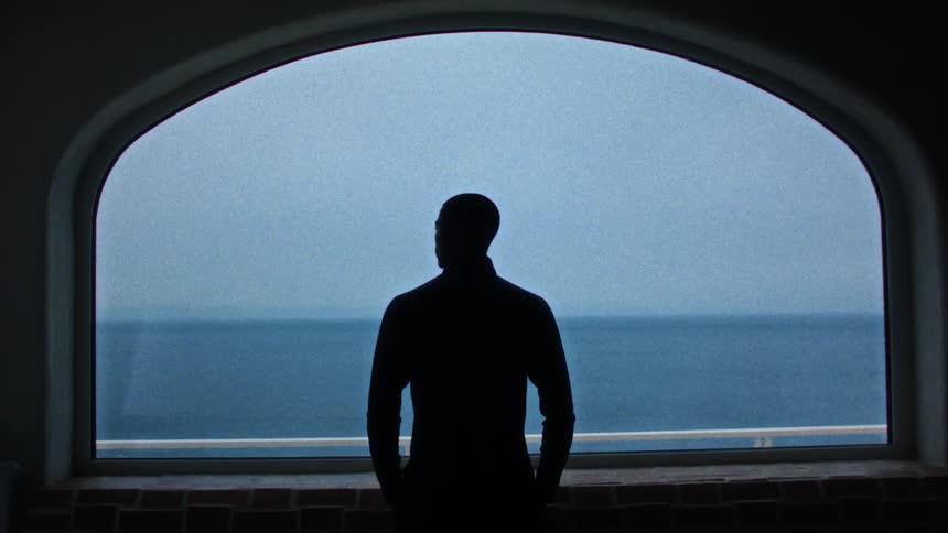 A man looking at the ocean through a large boat window