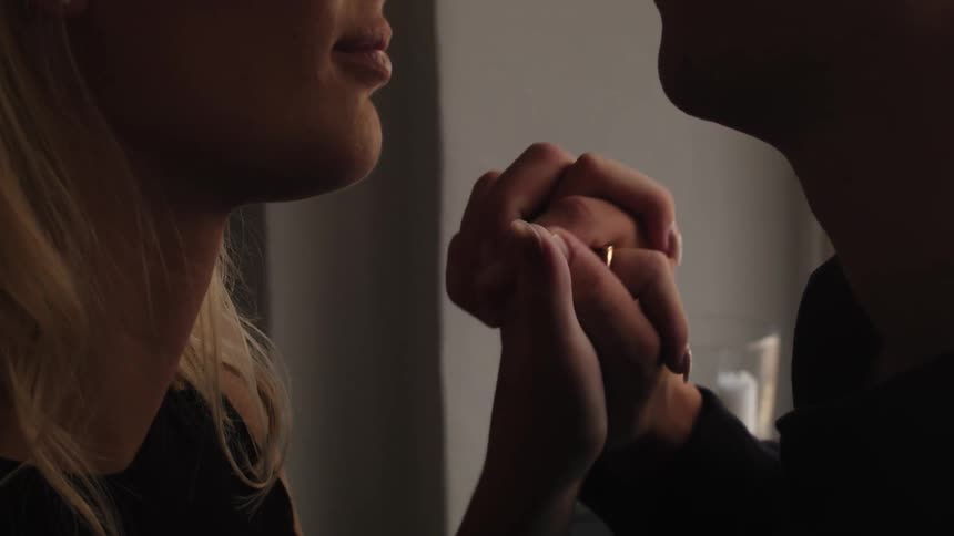 A young couple face each other while clasping hands romantically