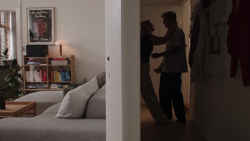 A couple is talking in the hallway of a living room and the woman pulls the man close to her