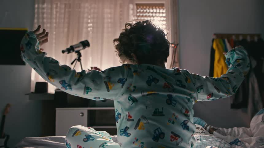 A boy stretches while sitting in his bed