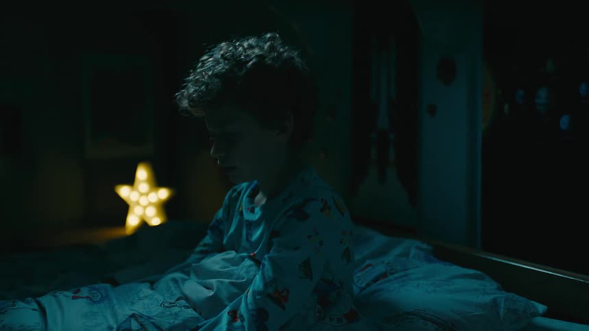 Boy sitting on bed breathing in the background at night