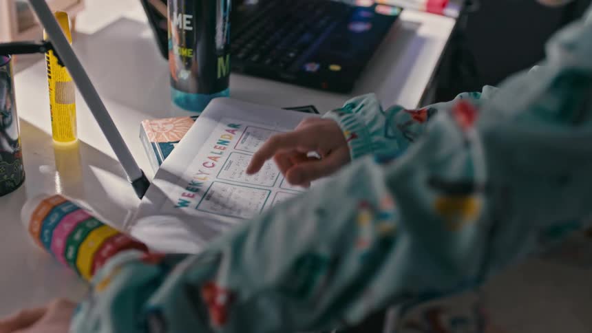 A child walks over to his desk and looks at a paper