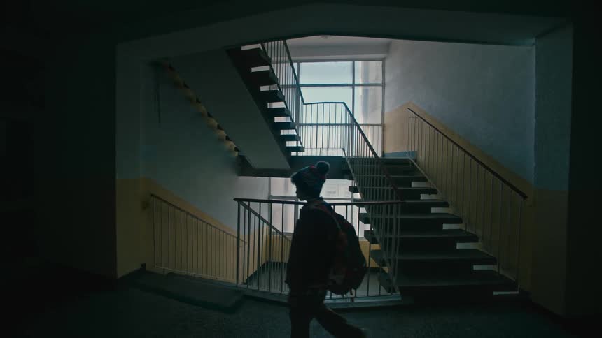 Young boy with a hat a denim jacket and black pants comes downstairs in a building