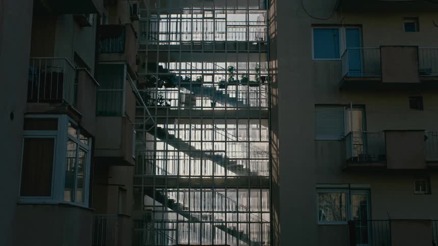 A person walking down an apartment building central staircase full of potted plants at morning