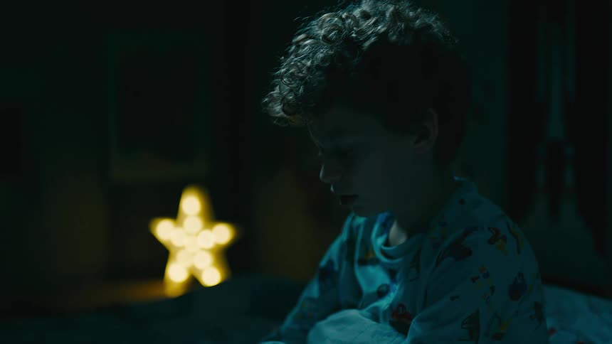 A child is sitting up in his bed at night