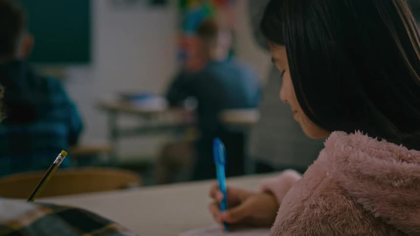 Portrait of a little boy talking to another little girl sitting at the school desk writing